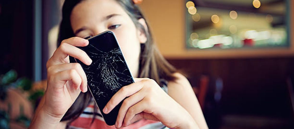 Young girl is watching her broken mobile phone after falling down.